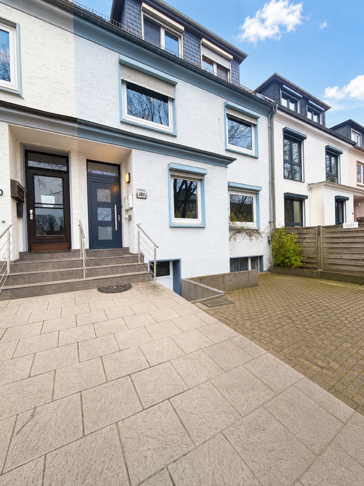 Helles Stadthaus mit blau abgesetzter Fassade und gepflastertem Vorplatz